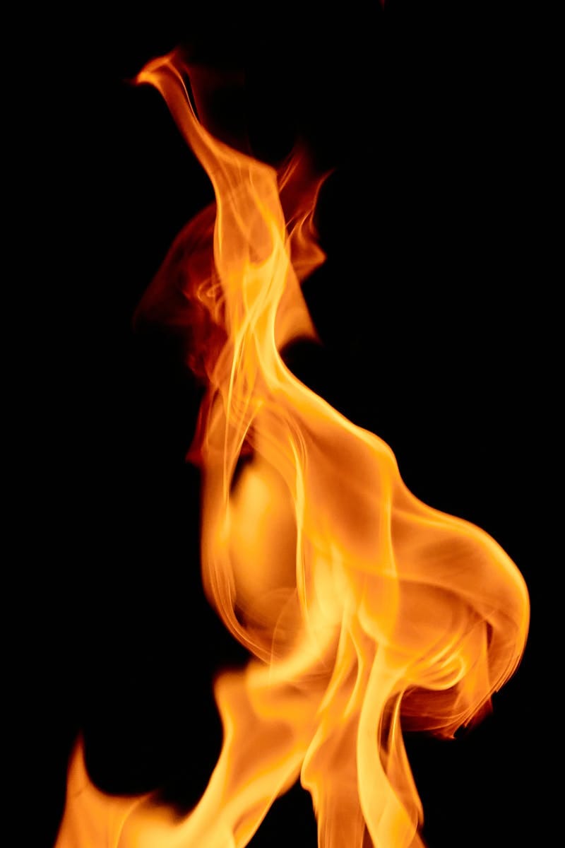 Captivating close-up of vibrant orange flames against a stark black background, showcasing the fluid dynamics of fire.